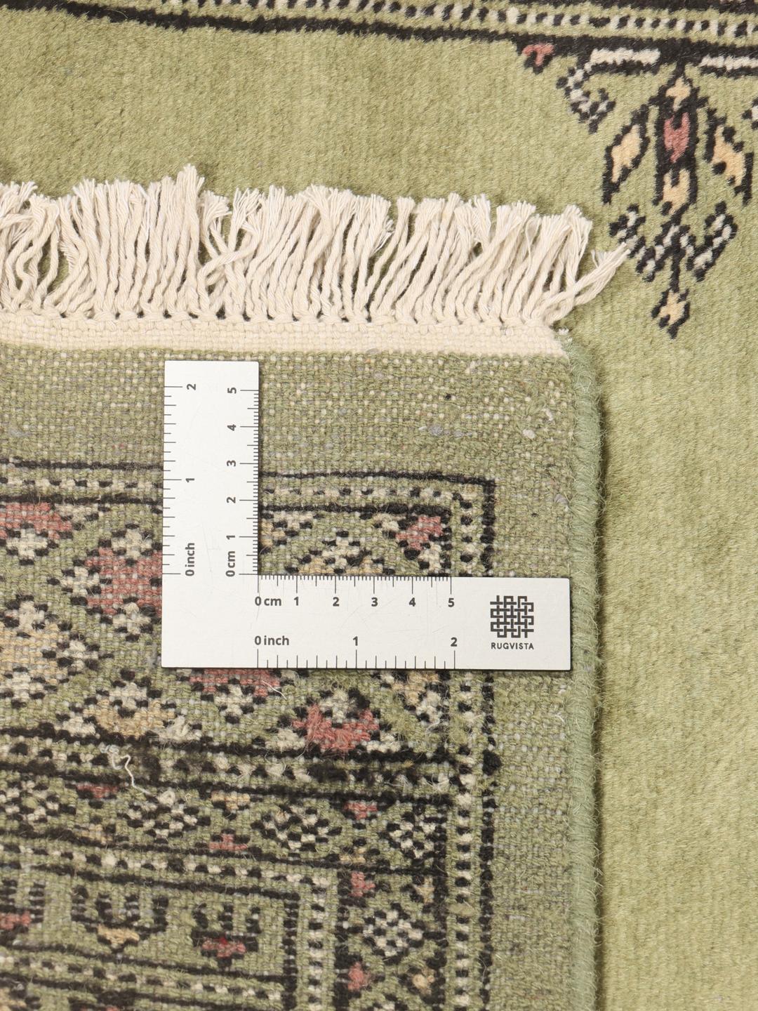 A long, narrow hand-knotted runner from Pakistan with a green field and traditional motifs.