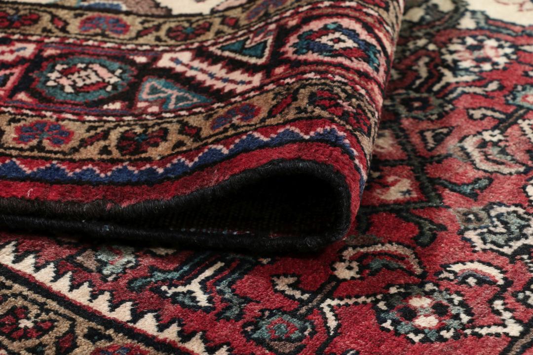 Handgeknoopt Nahavand-tapijt met een donkerrood veld en traditionele bloemmotieven.