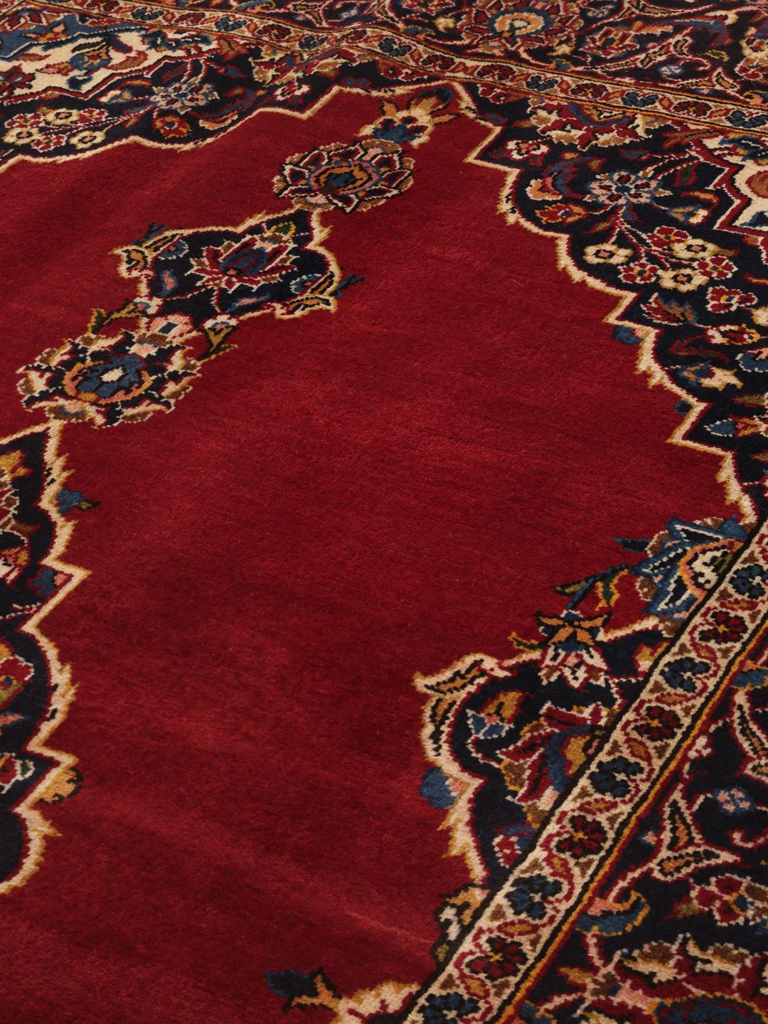 Een handgeknoopt Keshan tapijt uit het Midden-Oosten met een donkerrood veld en verfijnde florale details.