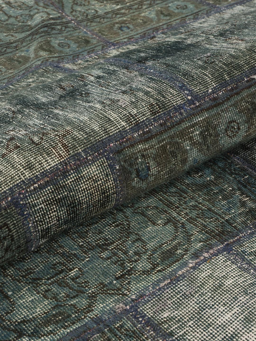Et rundt patchwork-tæppe i blå og grå nuancer med detaljerede håndknyttede tekstilfragmenter fra Mellemøsten.