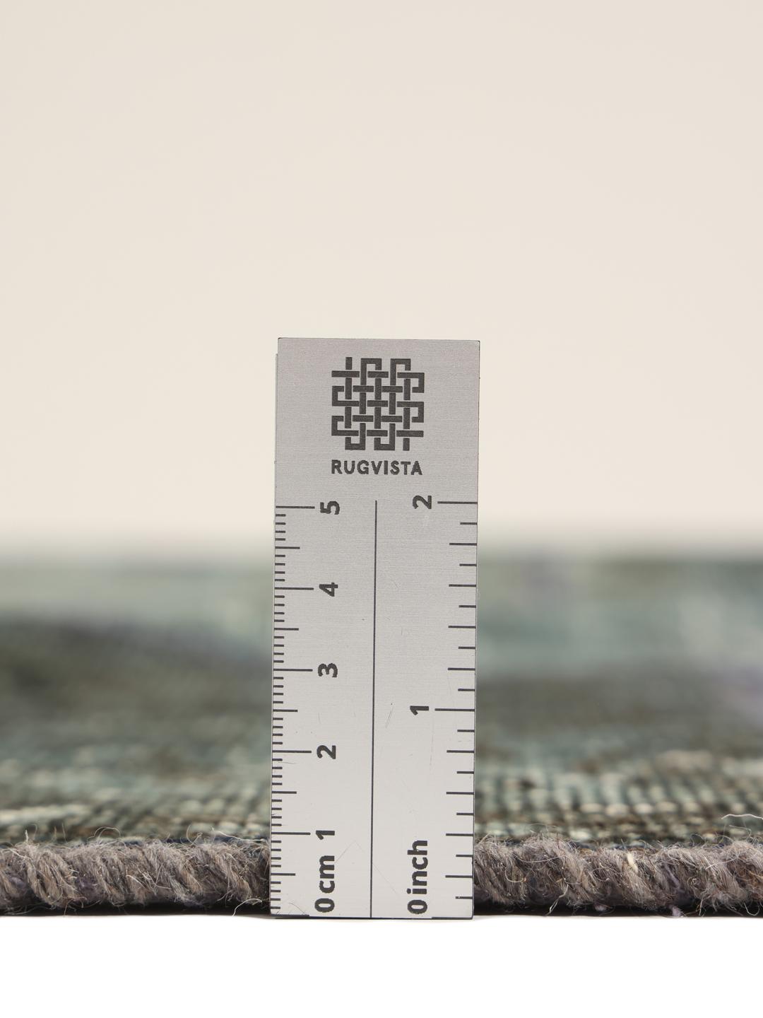 Et rundt patchwork-tæppe i blå og grå nuancer med detaljerede håndknyttede tekstilfragmenter fra Mellemøsten.