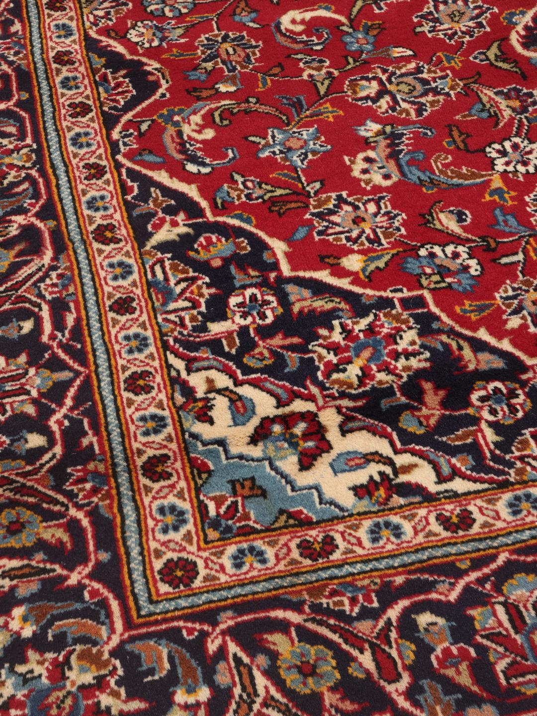 A hand-knotted Middle Eastern Keshan rug with a red and blue floral medallion design.
