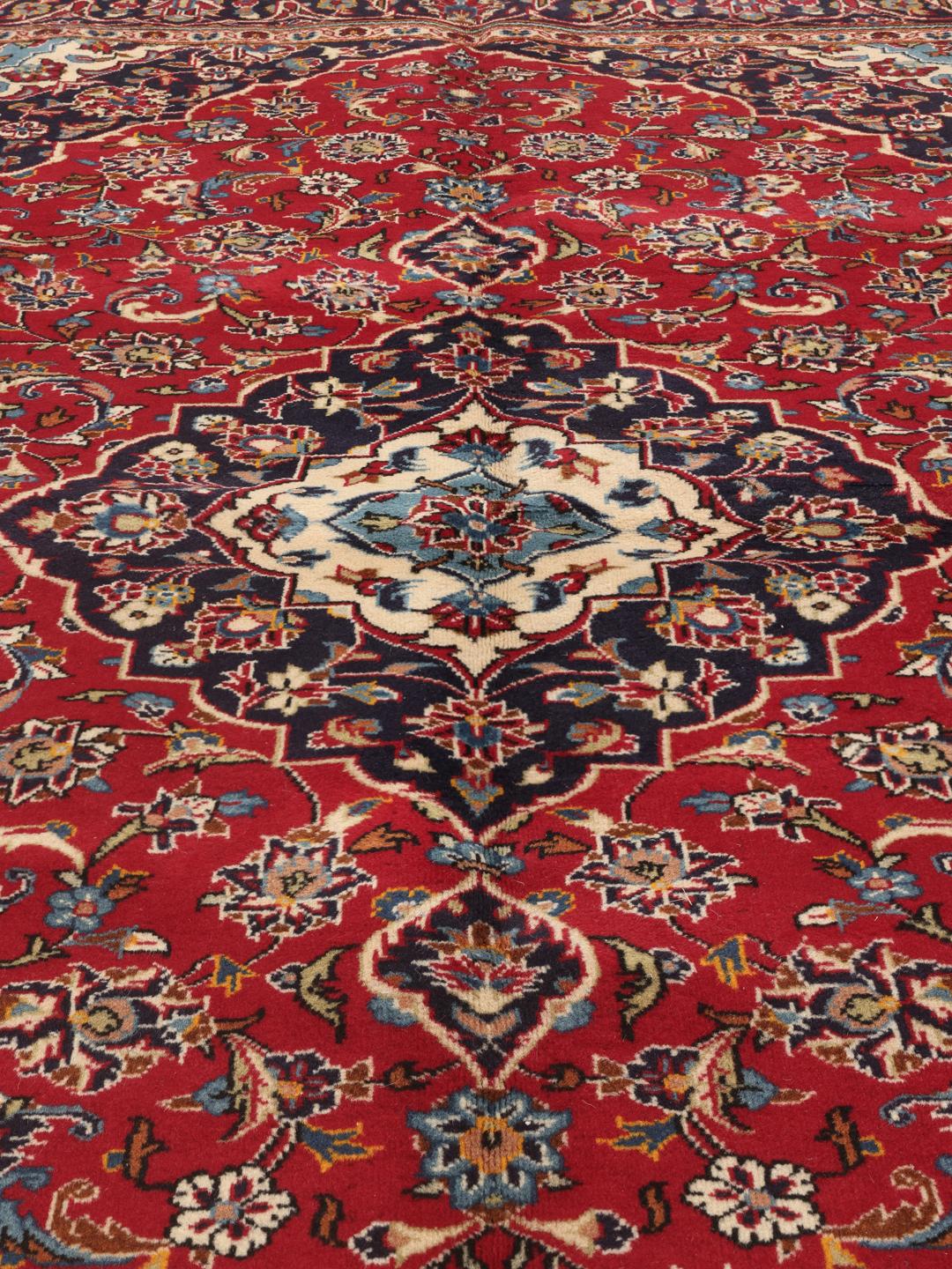 A hand-knotted Middle Eastern Keshan rug with a red and blue floral medallion design.