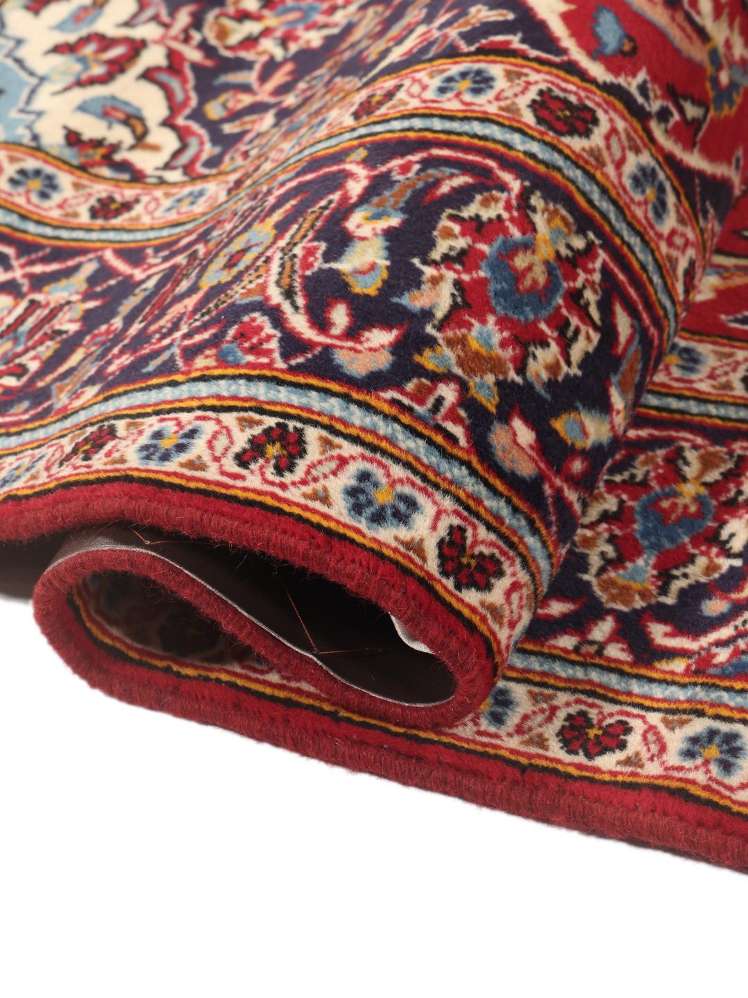 A hand-knotted Middle Eastern Keshan rug with a red and blue floral medallion design.