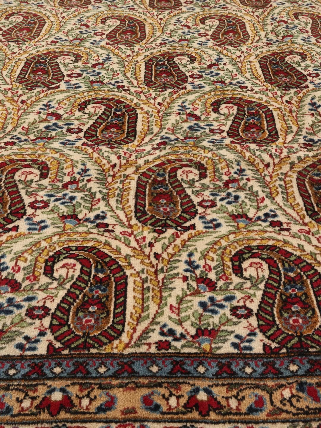 Een handgeknoopt Kerman tapijt uit het Midden-Oosten met een beige veld en rode en blauwe paisley-motieven.