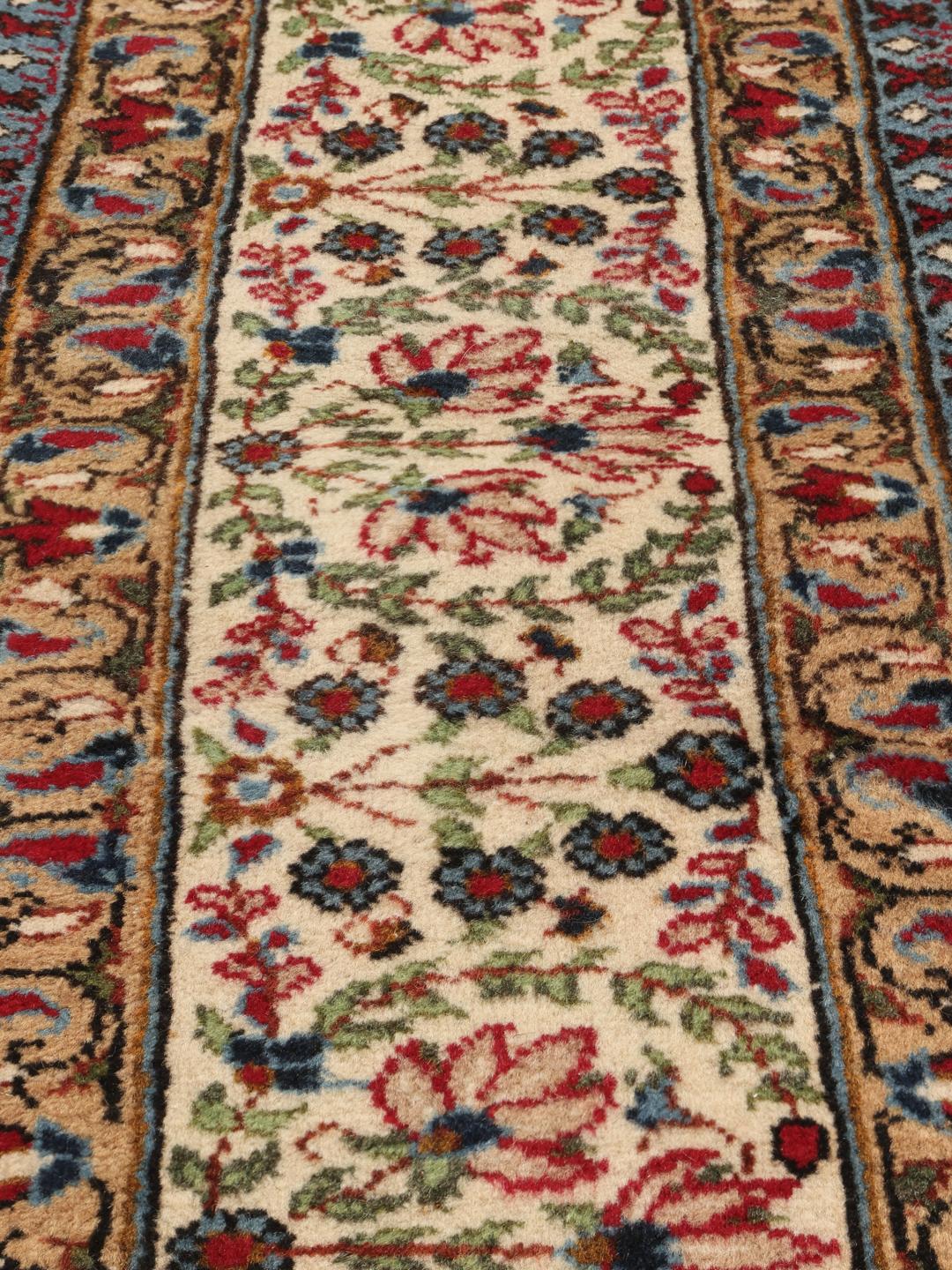 Een handgeknoopt Kerman tapijt uit het Midden-Oosten met een beige veld en rode en blauwe paisley-motieven.