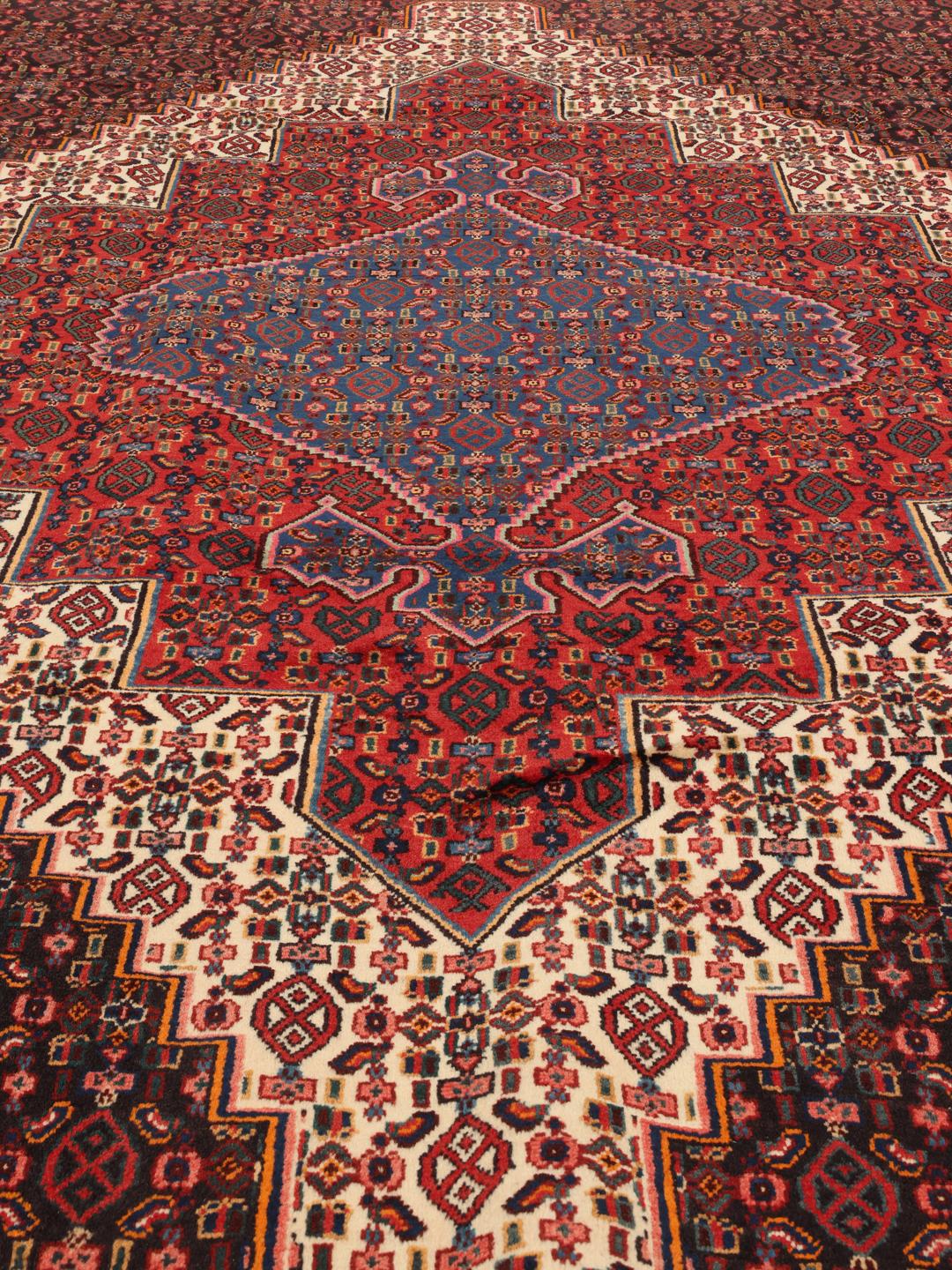 A hand-knotted Senneh rug from the Middle East featuring a dark-red and blue medallion design.