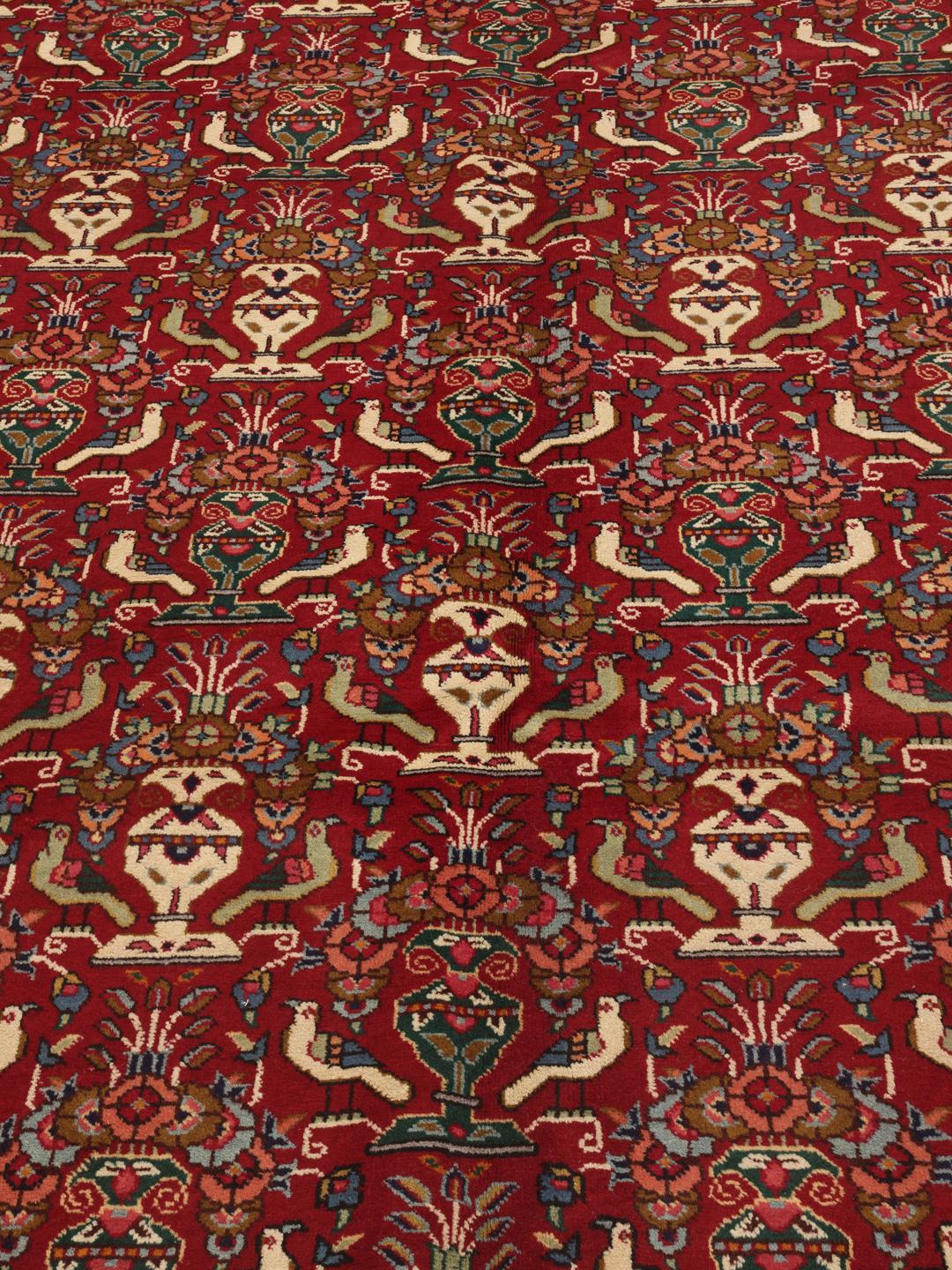 A large rectangular Tabriz rug with a deep red field and intricate floral motifs from the Middle East.