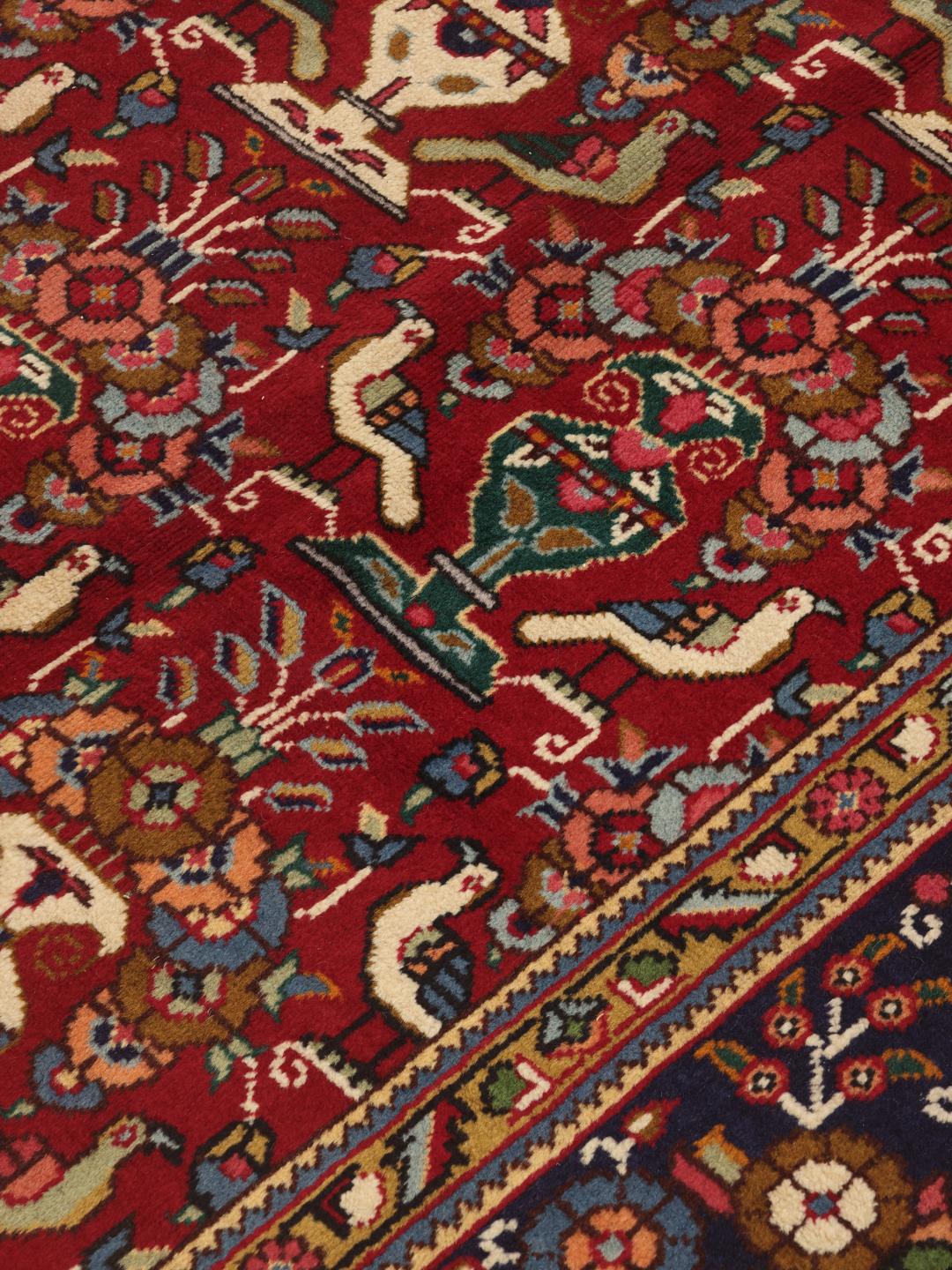 A large rectangular Tabriz rug with a deep red field and intricate floral motifs from the Middle East.