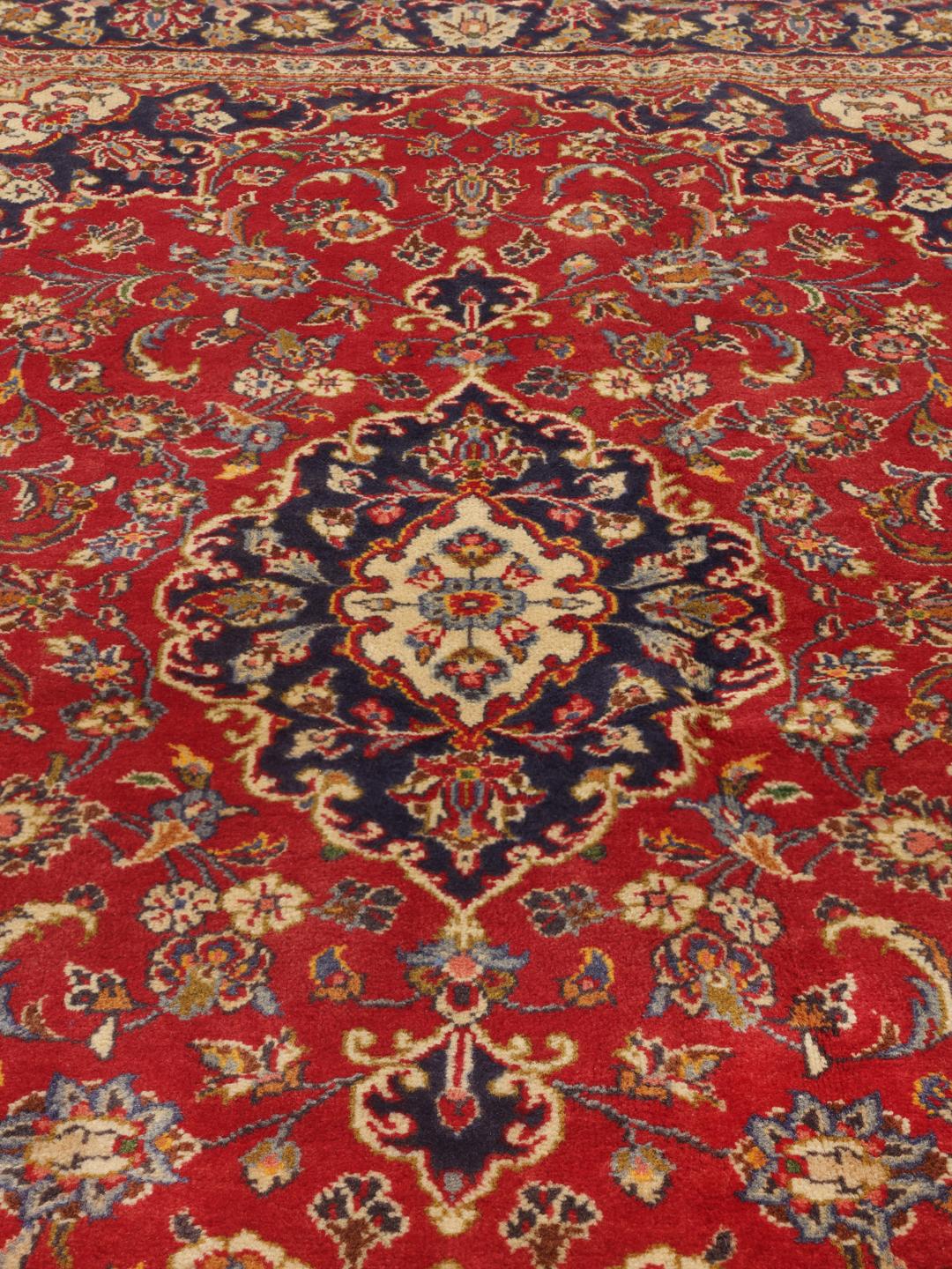 A hand-knotted Middle Eastern Keshan rug with a vibrant red and deep blue floral pattern.