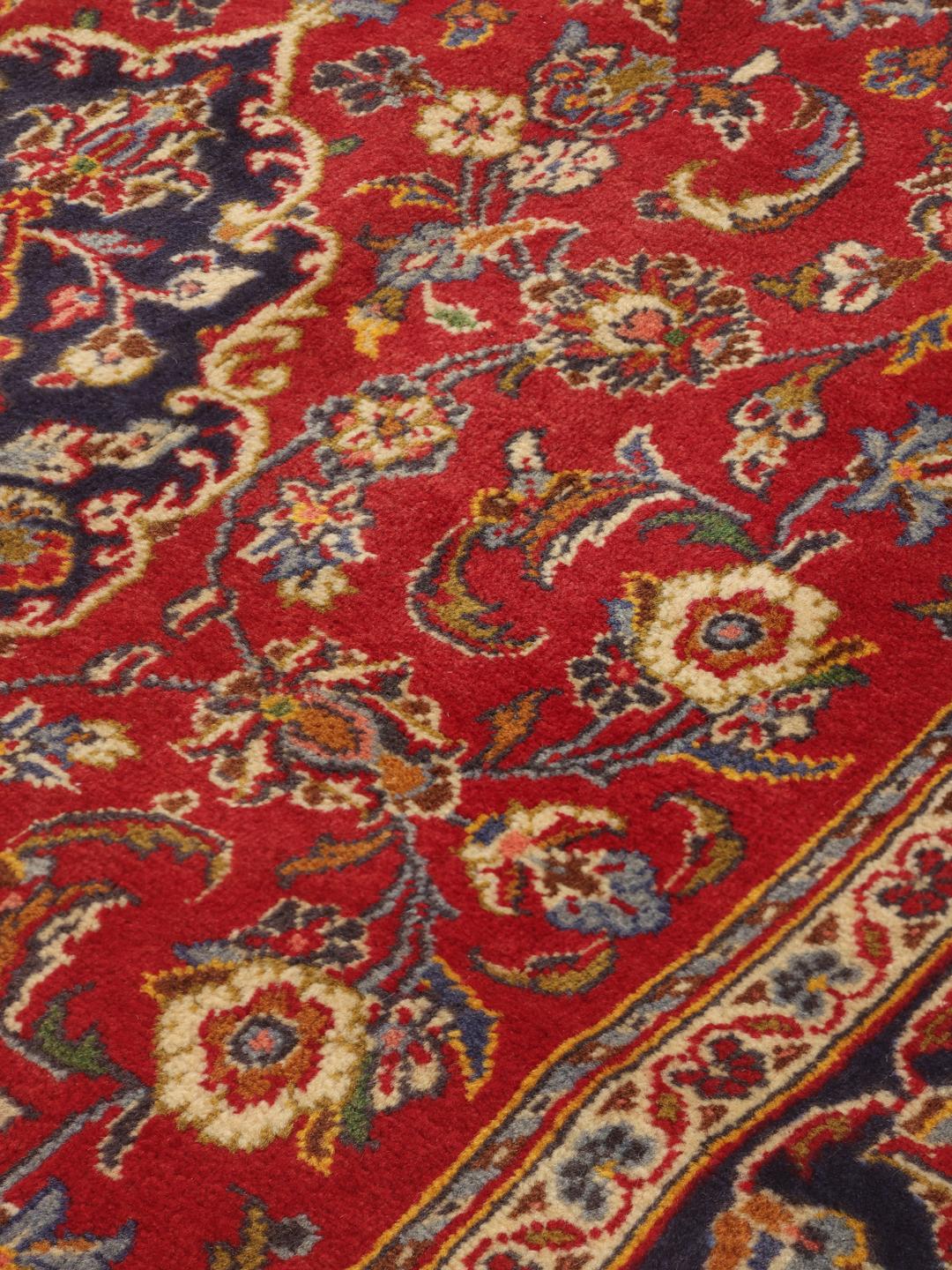 A hand-knotted Middle Eastern Keshan rug with a vibrant red and deep blue floral pattern.