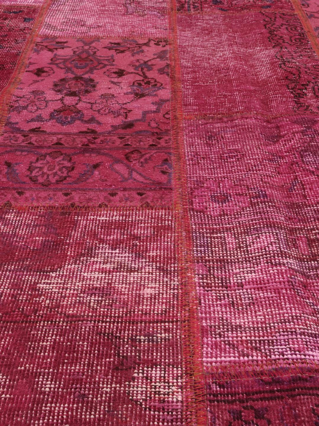 Een levendig roze patchwork tapijt van oorsprong uit het Midden-Oosten met gevarieerde handgeknoopte patronen.