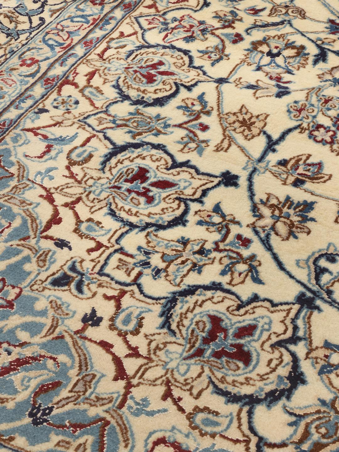 A large, rectangular Nain 9La rug with intricate blue and red floral patterns on a beige field, originating from the Middle East.