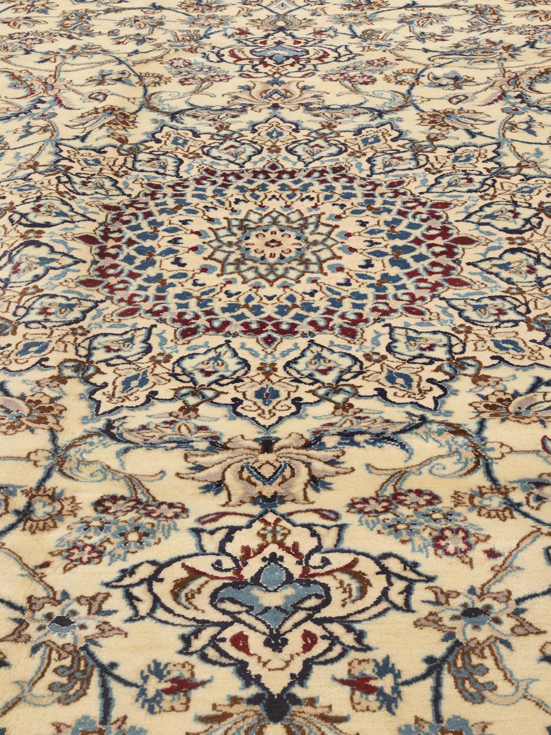 A large, rectangular Nain 9La rug with intricate blue and red floral patterns on a beige field, originating from the Middle East.