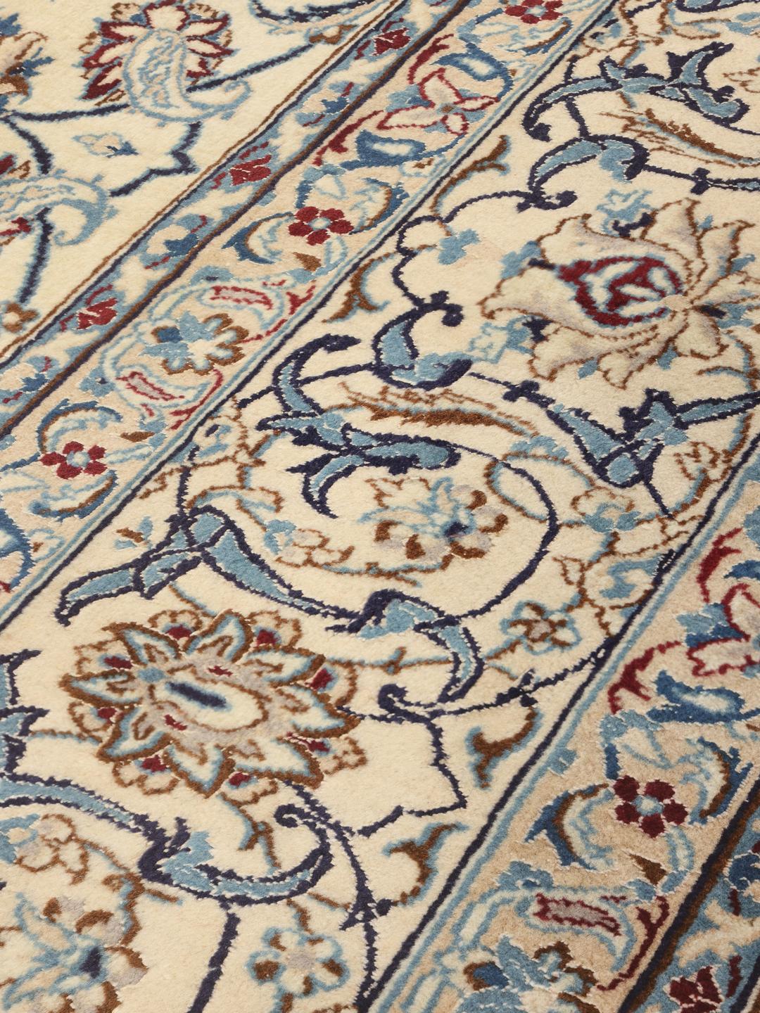 A large, rectangular Nain 9La rug with intricate blue and red floral patterns on a beige field, originating from the Middle East.