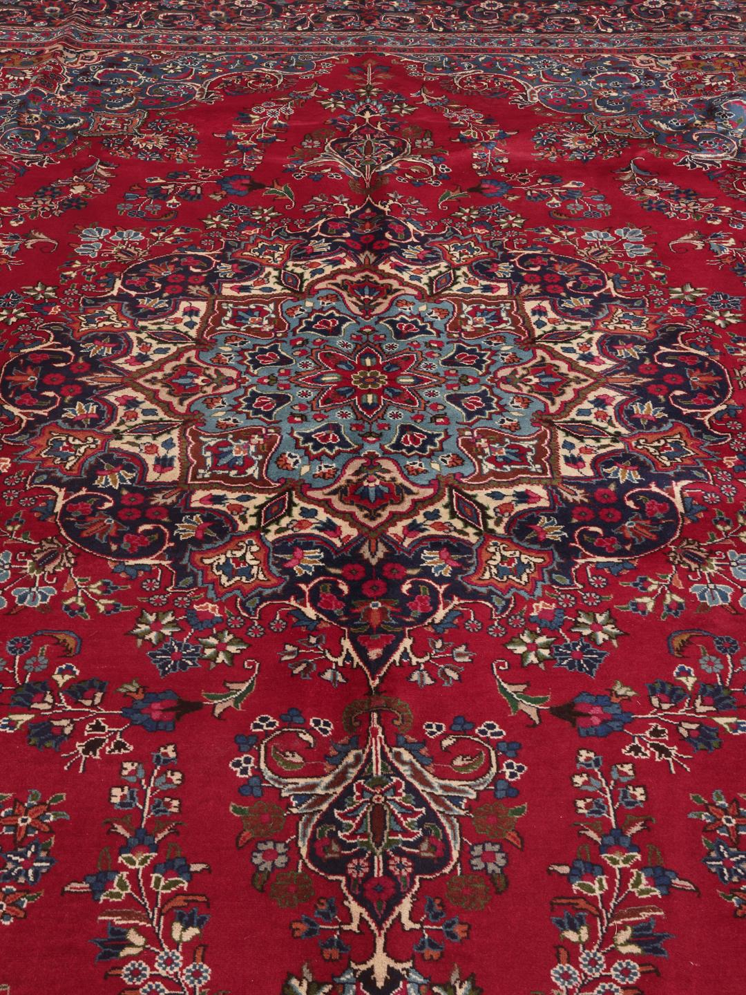 A large, hand-knotted Mashad rug from the Middle East in deep red and blue tones.