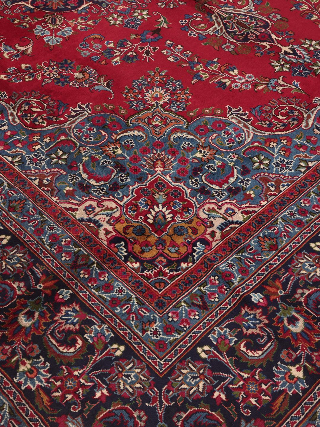 A large, hand-knotted Mashad rug from the Middle East in deep red and blue tones.