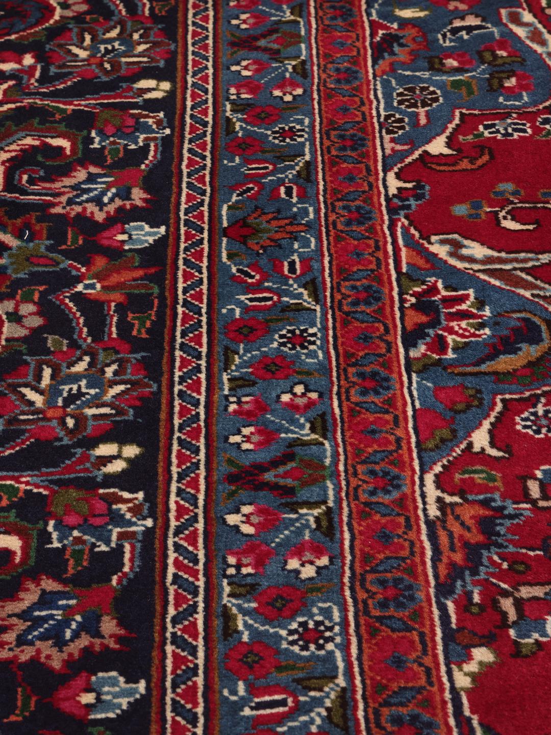 A large, hand-knotted Mashad rug from the Middle East in deep red and blue tones.