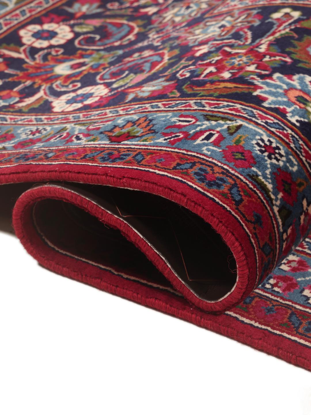 A large, hand-knotted Mashad rug from the Middle East in deep red and blue tones.