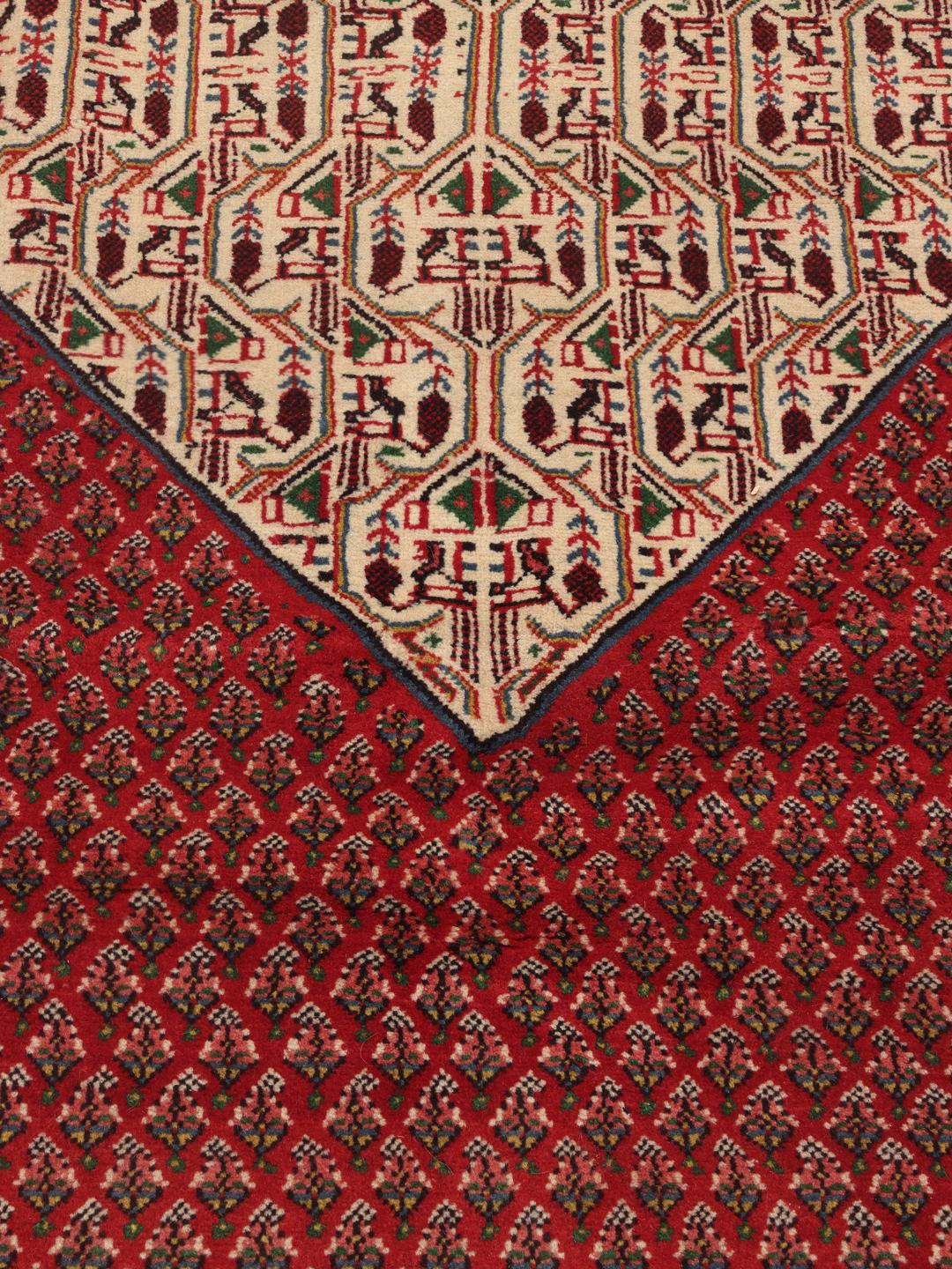 A large, hand-knotted Sarough Mir rug with a vibrant red field and geometric motifs.