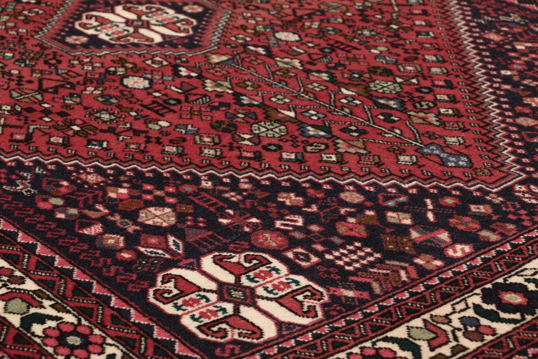 Et håndknyttet Abadeh-tæppe med en mørkerød bund og traditionelle geometriske motiver.