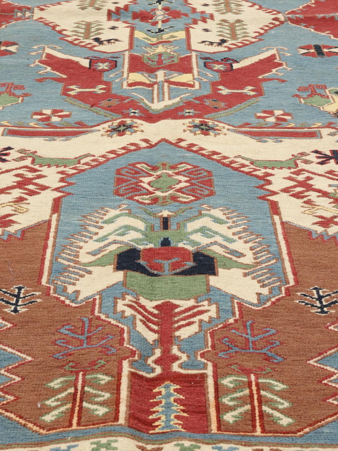Håndvævet afghansk Kelim-tæppe med blåt felt og ornamenterede geometriske motiver.