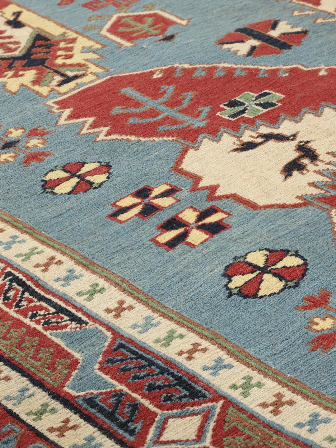 Håndvævet afghansk Kelim-tæppe med blåt felt og ornamenterede geometriske motiver.