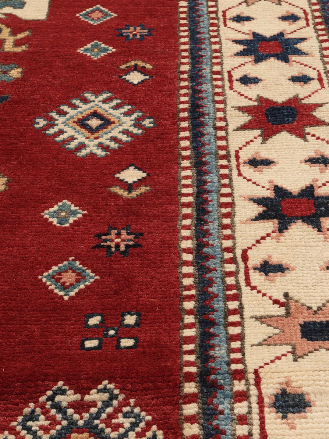 Tapis Kazak noué à la main en provenance d'Afghanistan avec un champ rouge et des motifs géométriques audacieux