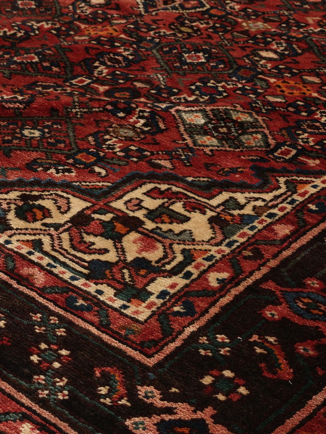 Et håndknyttet Hosseinabad-tæppe fra Mellemøsten med en rød flade og geometriske motiver.