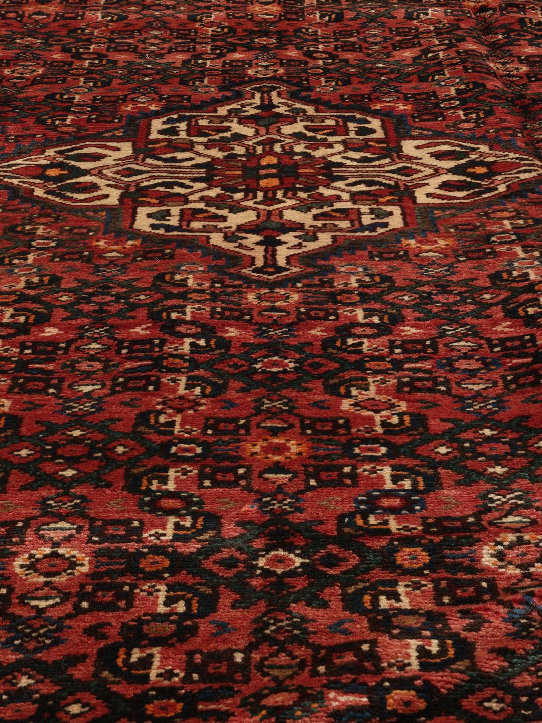 A hand-knotted Hosseinabad rug from the Middle East featuring a dark-red field and intricate patterns.