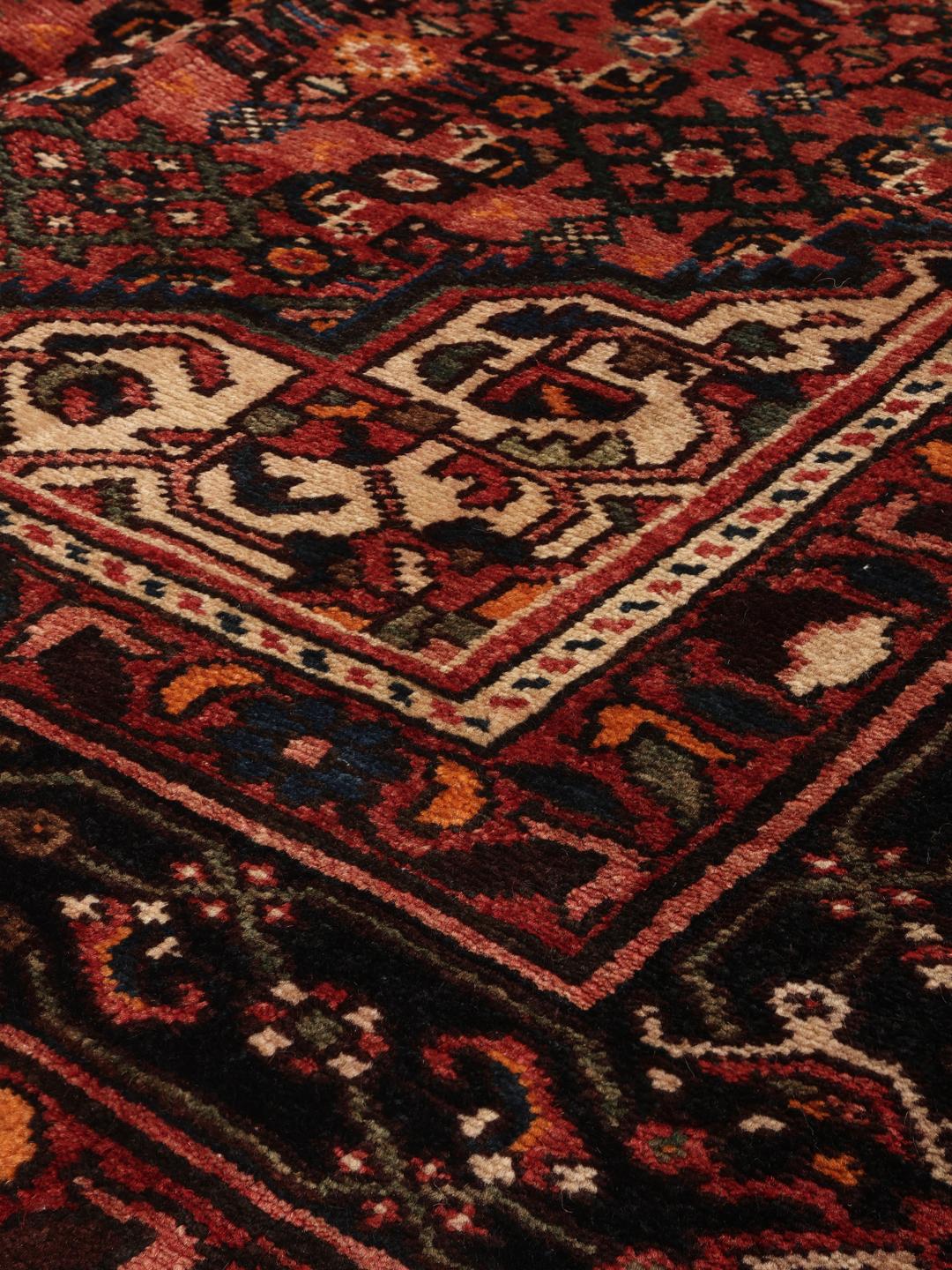 A hand-knotted Hosseinabad rug from the Middle East featuring a dark-red field and intricate patterns.