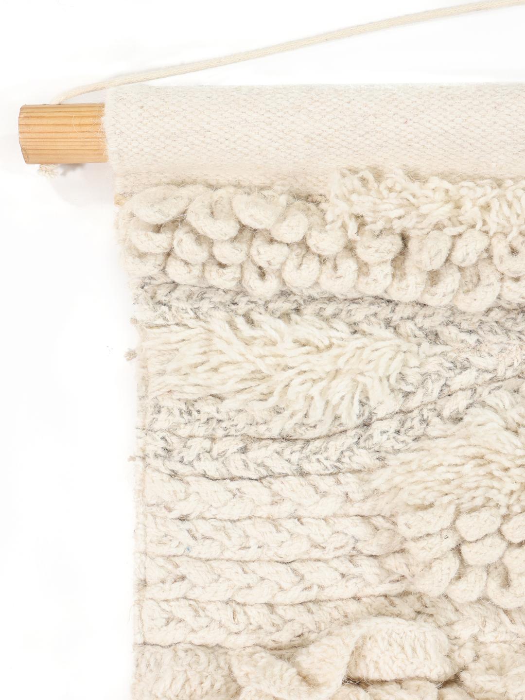 Een handgeweven witte en veelkleurige wanddecoratie met getextureerde lagen.