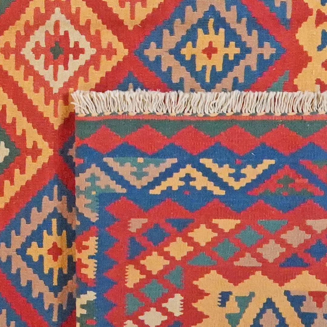 Et levende, håndvævet Kilim Qashqai-tæppe fra Mellemøsten med et dristigt rødt, blåt og gult geometrisk mønster.