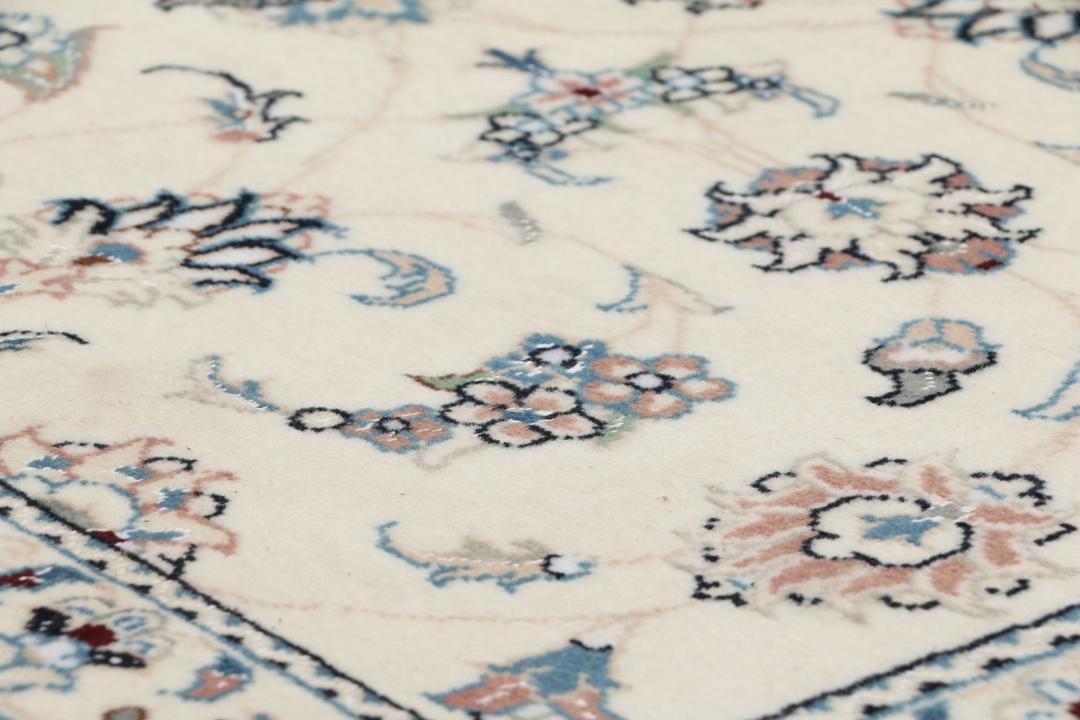 Een rechthoekig handgeknoopt Nain 9La tapijt uit het Midden-Oosten met een beige achtergrond en bloempatronen in blauw en roze.