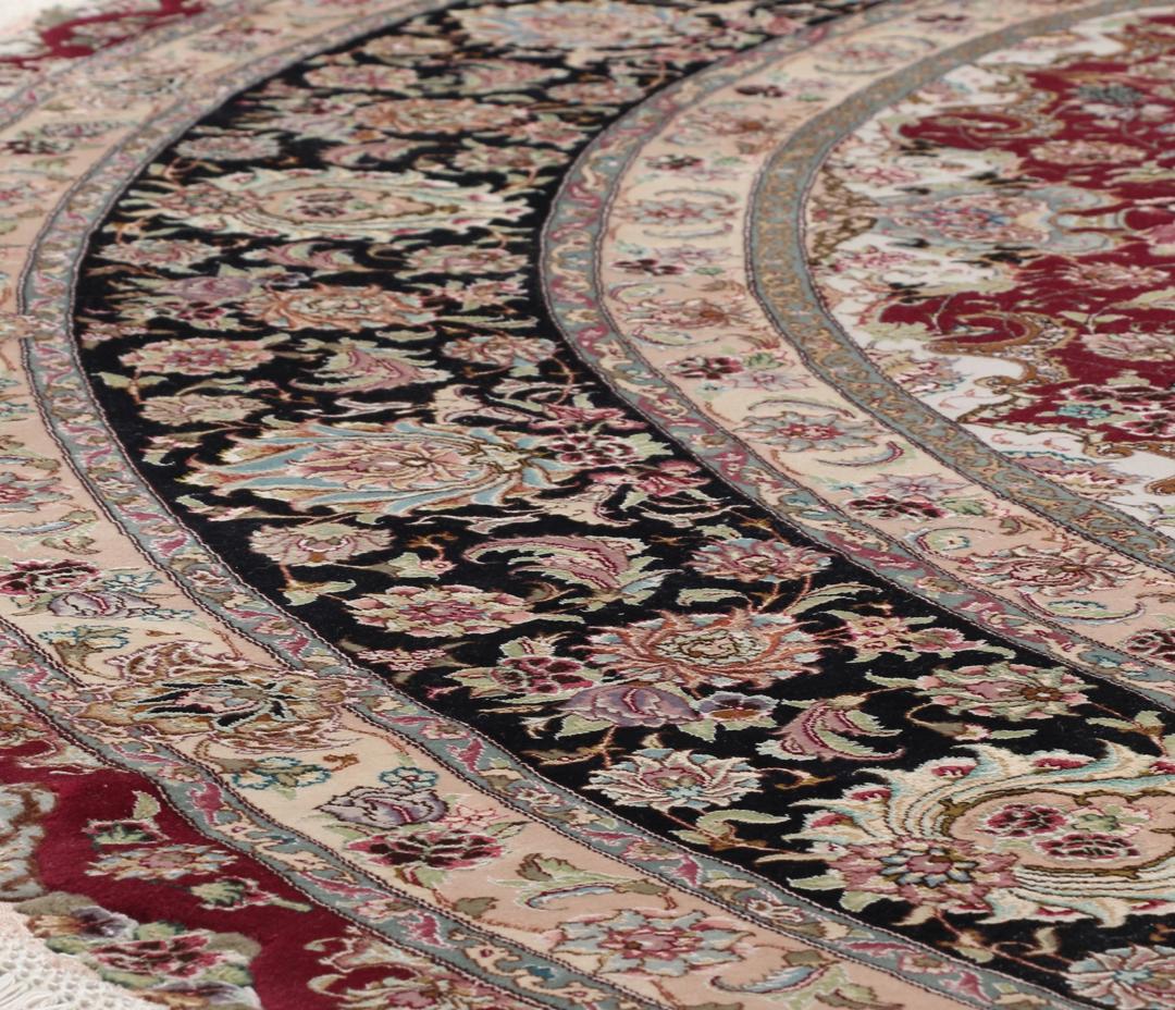 Een rond, handgeknoopt Tabriz-tapijt uit het Midden-Oosten met een levendig rood en zwart bloemendesign.