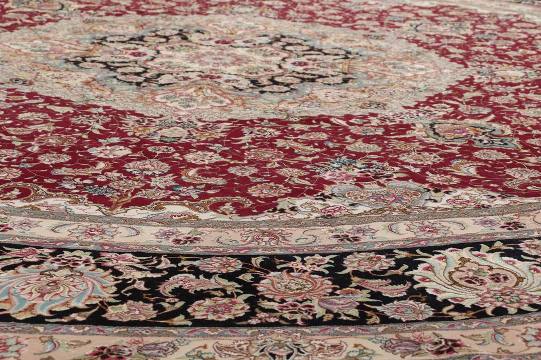 Een rond, handgeknoopt Tabriz-tapijt uit het Midden-Oosten met een levendig rood en zwart bloemendesign.