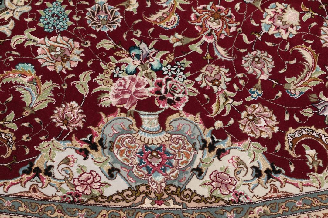 Een rond, handgeknoopt Tabriz-tapijt uit het Midden-Oosten met een levendig rood en zwart bloemendesign.