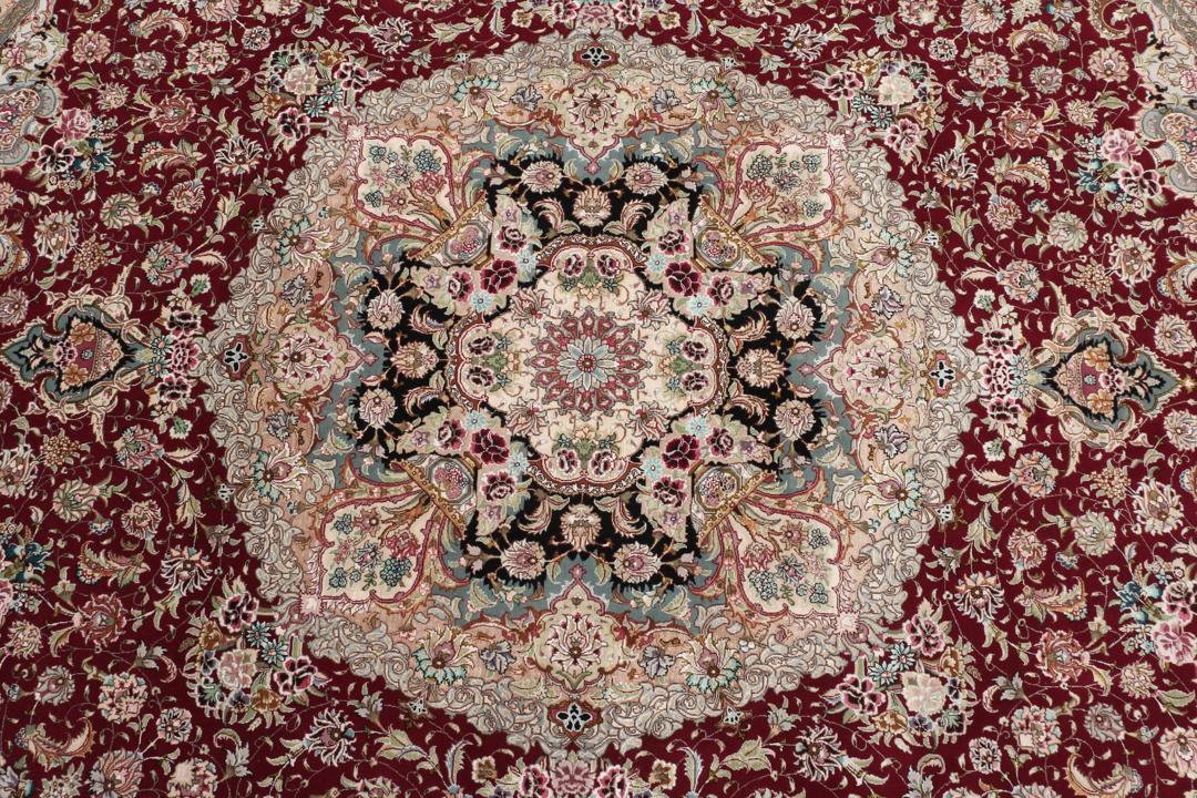 Een rond, handgeknoopt Tabriz-tapijt uit het Midden-Oosten met een levendig rood en zwart bloemendesign.