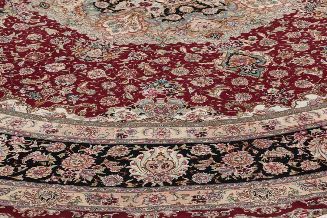 Een rond, handgeknoopt Tabriz-tapijt uit het Midden-Oosten met een levendig rood en zwart bloemendesign.