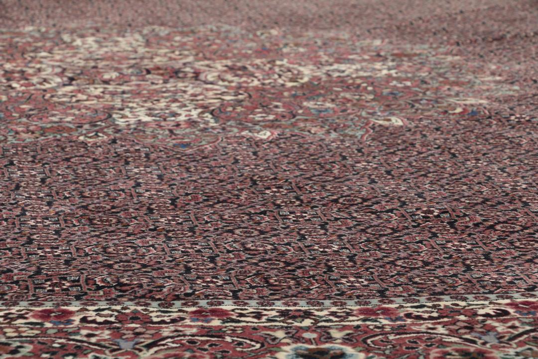 Et stort rundt, unikt Bidjar-tæppe med en dyb mørkerød bund og indviklede blomstermotiver.