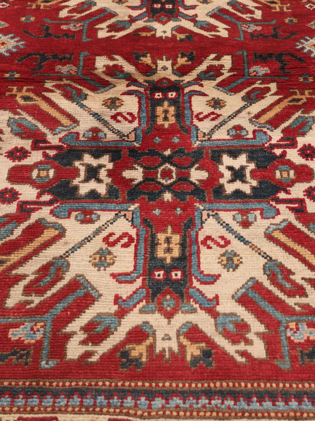 Een handgeknoopt Afghaans Kazak tapijt met gedurfde geometrische rode, blauwe en crèmekleurige motieven.