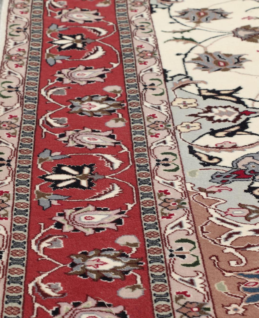 Un tapis Tabriz noué à la main provenant du Moyen-Orient avec un médaillon floral rouge sur fond crème.