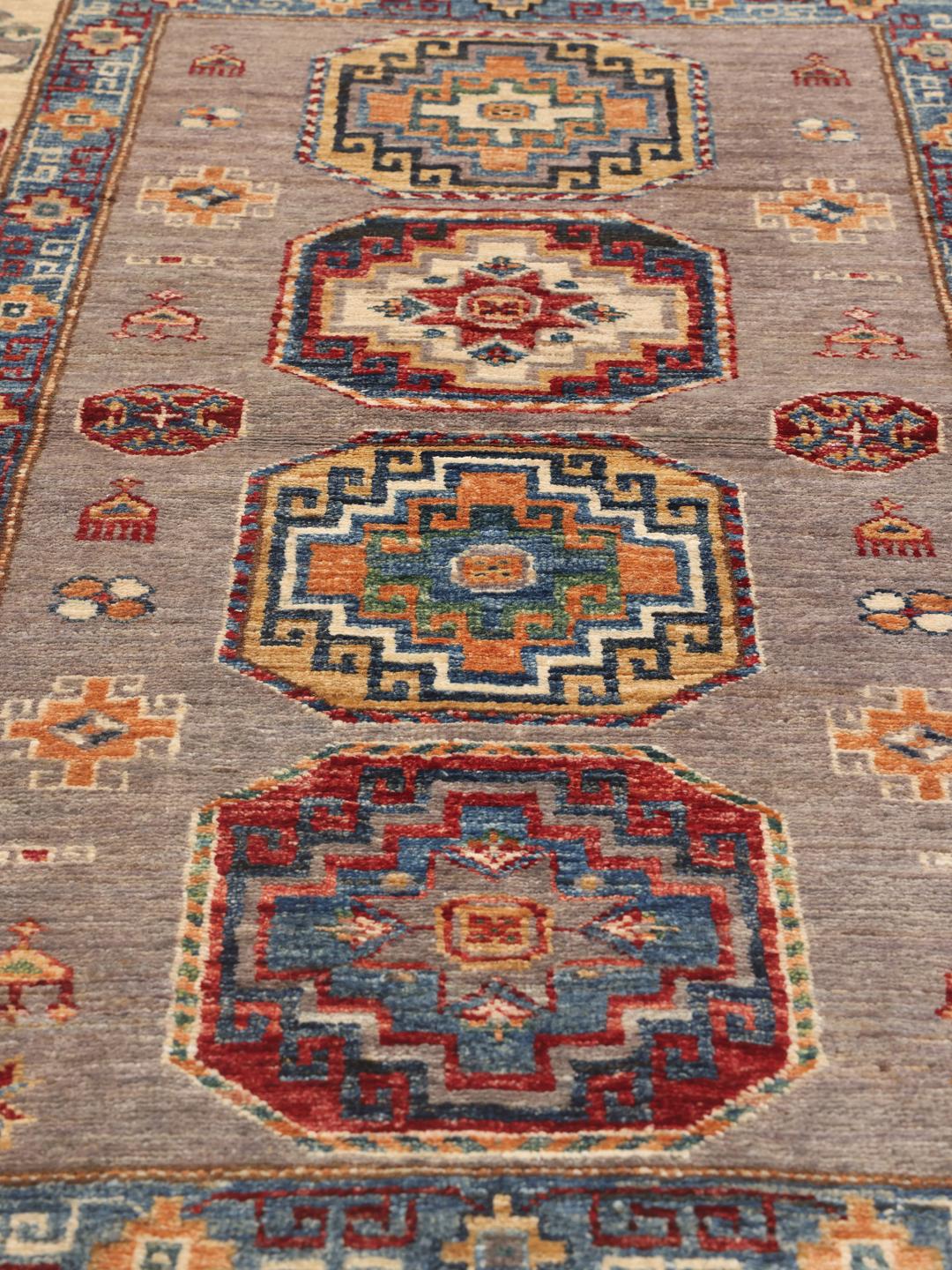 Een rechthoekig handgeknoopt Kazak tapijt uit Afghanistan met gedurfde geometrische medaillons op een grijs veld.