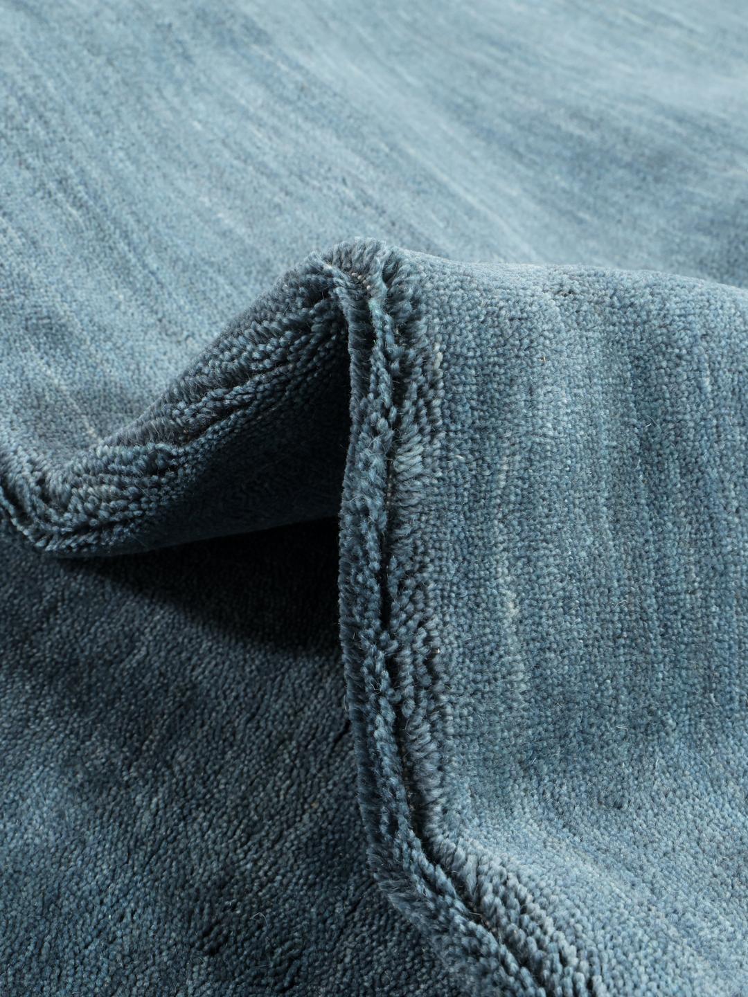 Et ensfarvet mørkegrønt håndvævet tæppe med korte matchende frynser