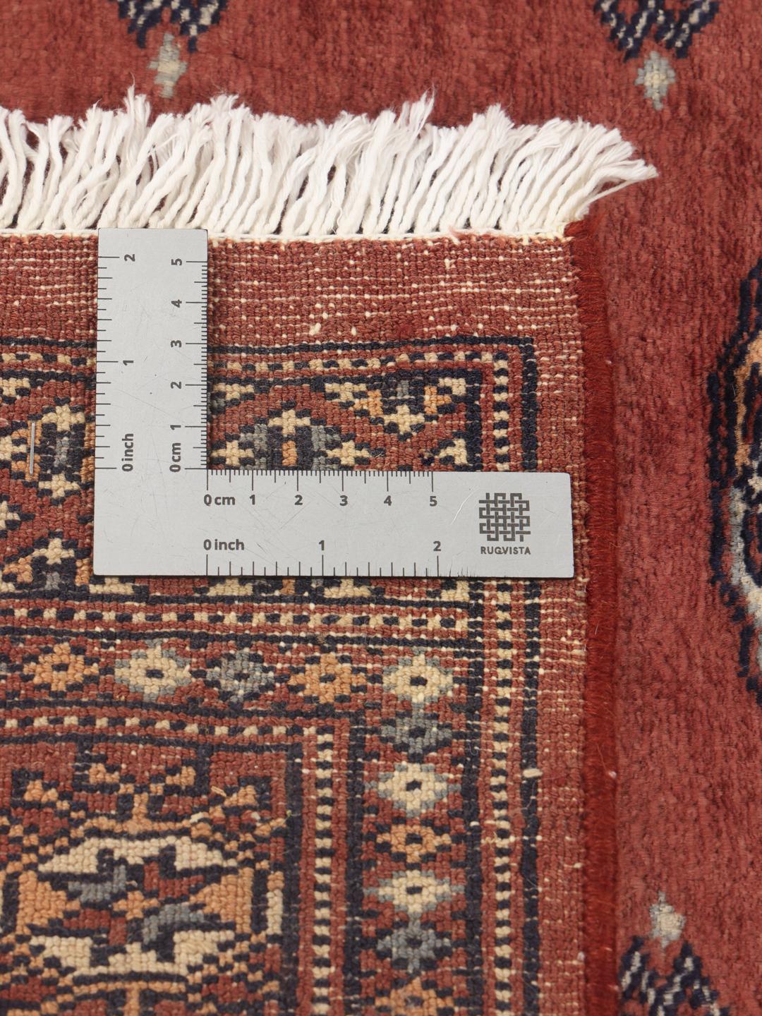 Een rechthoekig handgeknoopt Pakistan Bokhara tapijt met een dieprood veld en herhalende geometrische motieven.