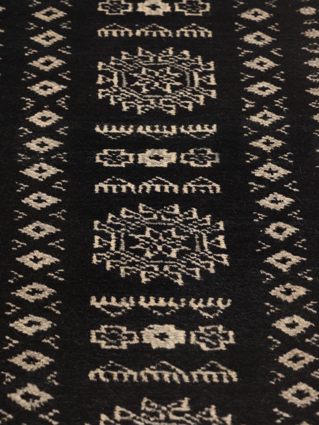 A hand-knotted black Pakistan Bokhara rug with traditional geometric motifs.