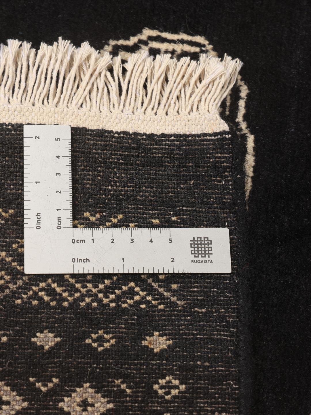 A hand-knotted black Pakistan Bokhara rug with traditional geometric motifs.