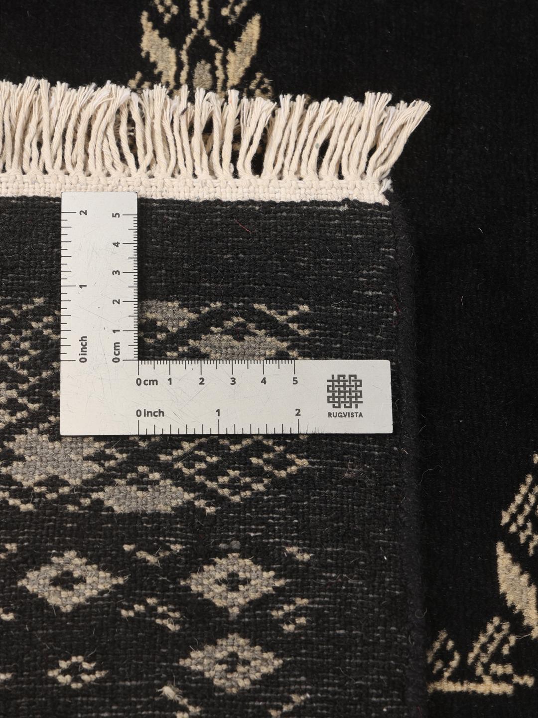 A hand-knotted Pakistan Bokhara rug in black with detailed geometric motifs.