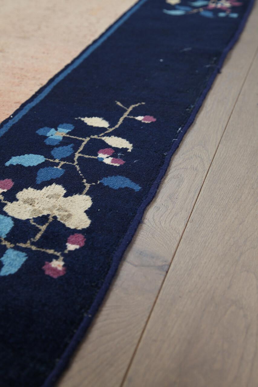 Antikt kinesisk tæppe med blomstermotiver på en beige baggrund og mørk kant