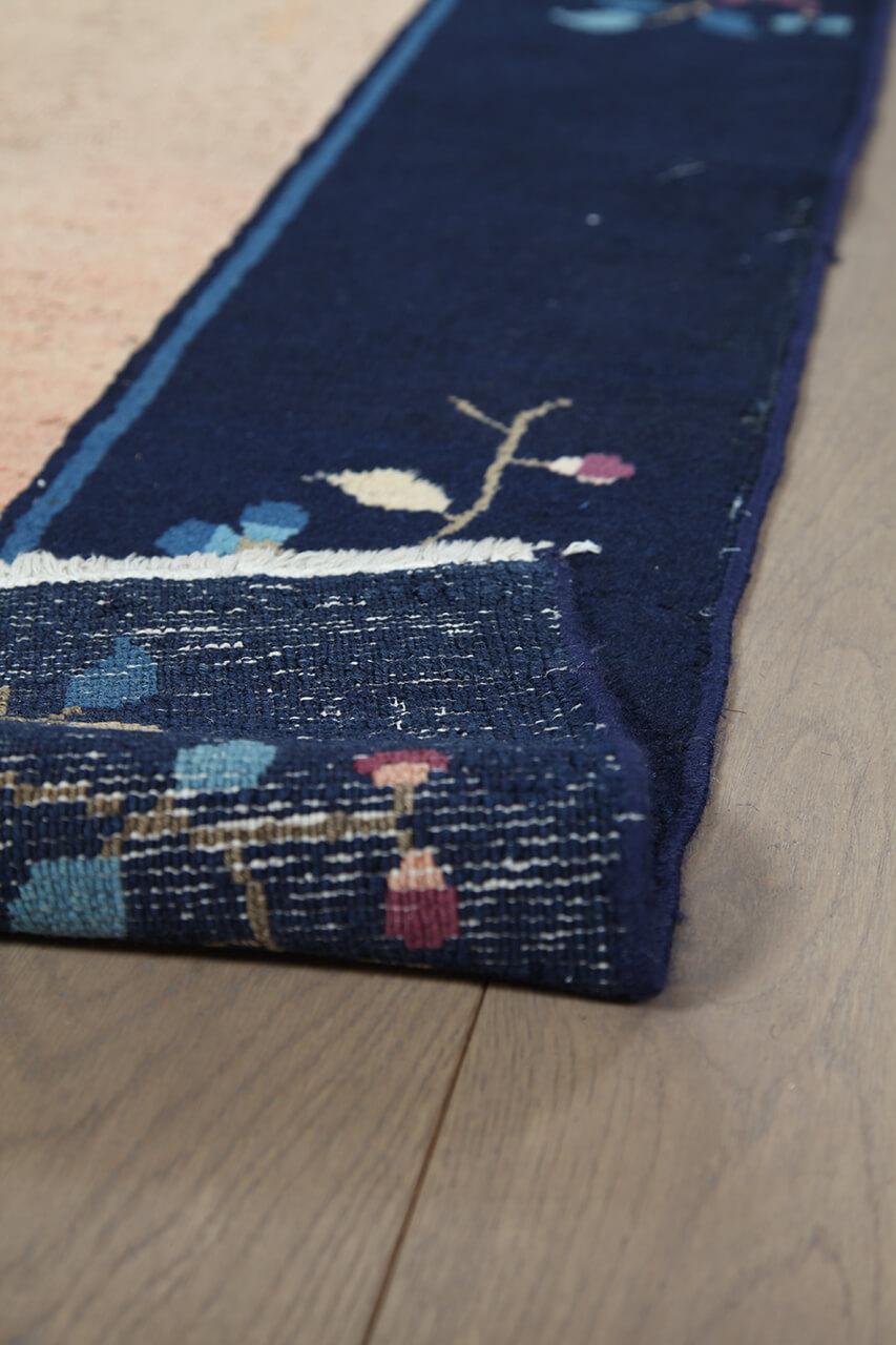 Antikt kinesisk tæppe med blomstermotiver på en beige baggrund og mørk kant